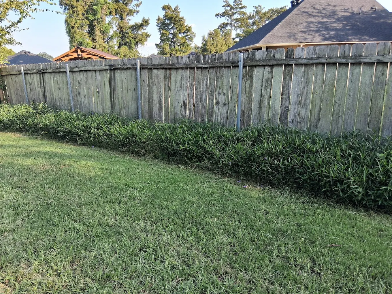 Side-by-side comparison of a backyard showing before and after stone patio installation behind a two-story house with wooden steps and a screened porch.