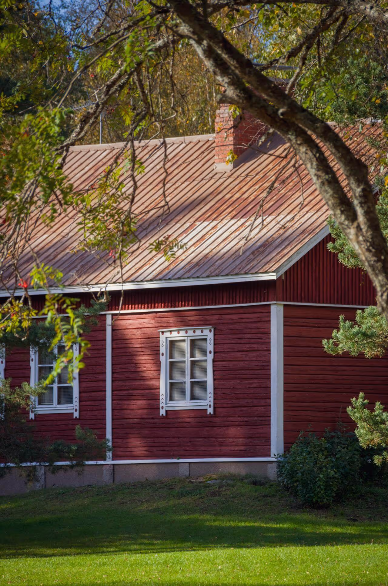 Construction site with workers assembling a gray concrete block retaining wall beside a house, surrounded by trees and gravel.