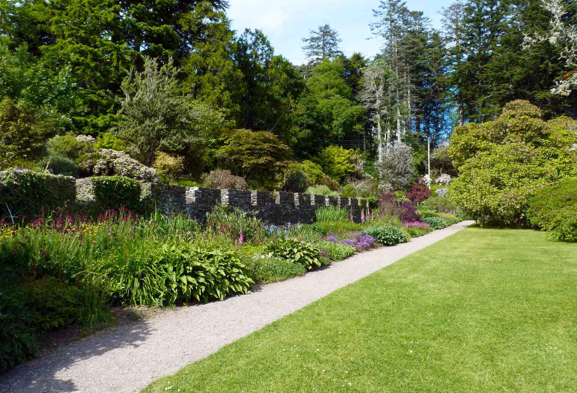 Side-by-side comparison of a backyard showing before and after stone patio installation behind a two-story house with wooden steps and a screened porch.